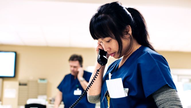 Two nurses speaking on desk phones.
